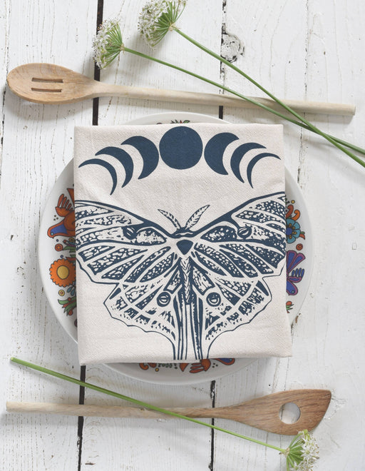 Hearth and Harrow - Organic Cotton Luna Moth Tea Towel displayed on a floral plate, accompanied by wooden spoons and wildflowers, showcasing eco-friendly kitchen elegance.