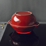 Emile Henry Bread Pot on a cooktop, showcasing its two-piece ceramic design for even heat. Nearby, bay leaves hint at culinary possibilities.