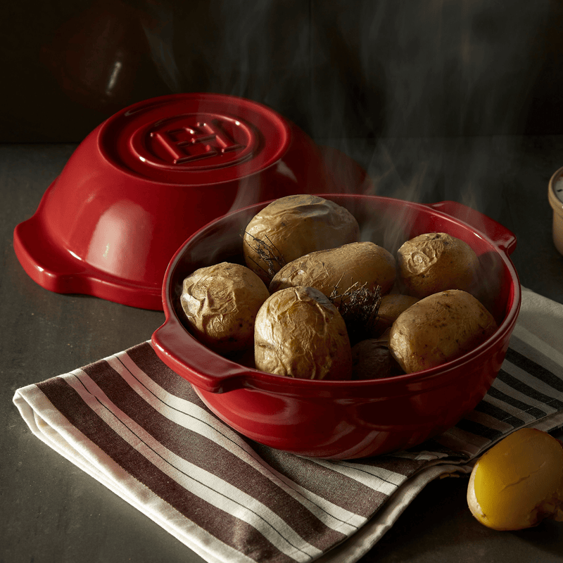 Emile Henry | Bread Pot, Charcoal, showcasing steaming, baked potatoes with herbs, on a striped cloth, highlighting its even heat distribution for perfect roasting.