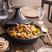 Emile Henry Tagine, Ocean, is showcased in a North African-style setting with a flavorful stew, flatbreads, and brass ladle, emphasizing its unique cooking design.