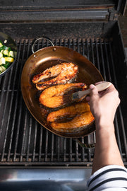 de Buyer | Oval Roasting Pan in use, grilling fish on an outdoor barbecue, showcasing its versatility for cooking meat and seafood.