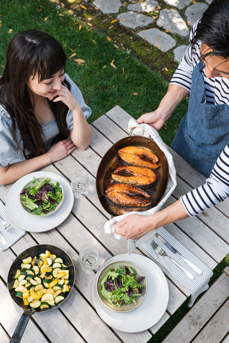 Woman holding de Buyer | Oval Roasting Pan with cooked fish and vegetables, showcasing the pan's versatility for roasting and serving directly to guests.