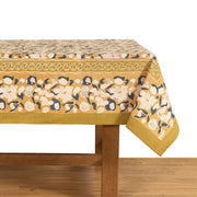 Couleur Nature - Forest Harvest Mustard & Blue tablecloth featuring floral motifs on a wooden table, showcasing artisan craftsmanship and rich Provençal-inspired design.