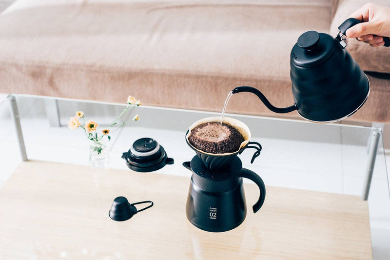 HARIO USA - V60 Metal Dripper: Silver in a pour-over setup, with a black gooseneck kettle pouring into the dripper atop a matching server.