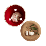 Emile Henry | Garlic Pot, Burgundy, with ventilation holes for storage, paired with a cork board displaying garlic cloves, bay leaves, and thyme.