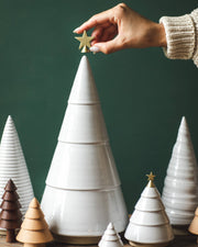 Farmhouse Pottery - Balsam Woodland Trees: Medium. Hand places star on ceramic tree, surrounded by smaller wood and ceramic trees, showcasing elegant, year-round decor versatility.