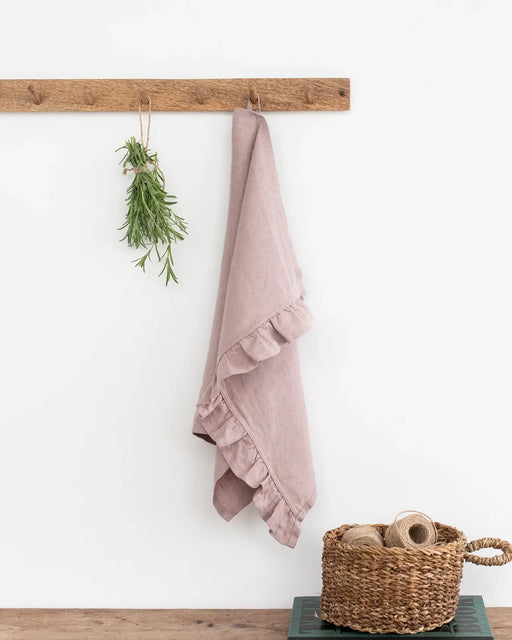 Linen tea towel with ruffle trim hanging on a hook, showcasing its texture and practicality, part of MagicLinen's durable and absorbent kitchen collection.