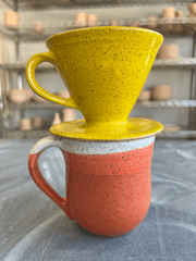 Handmade speckled ceramic mug with red and white glaze, stacked with a yellow cone-shaped coffee pour-over from RachaelPots, suitable for filters, perfect for kitchen enthusiasts.