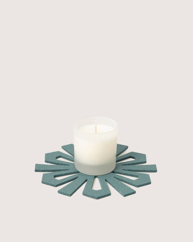 Graf Lantz - Merino Wool Snowflake Trivet - Heather Spruce in teal-blue felt, under a small candle in a clear glass vessel, offering both elegance and surface protection.