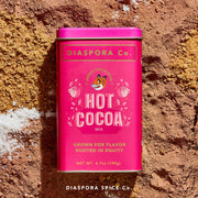 Diaspora Spices Co. Hot Cocoa Mix tin on cocoa powder, showcasing Grown for Flavor, Rooted in Equity label with tiger illustration, promising velvety, naturally-sweetened hot chocolate.