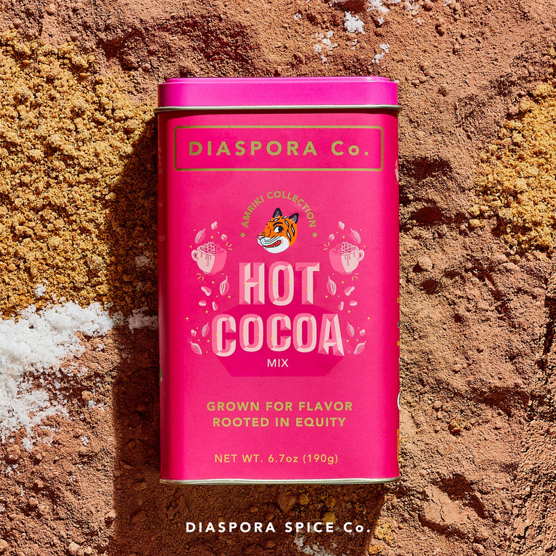 Diaspora Spices Co. Hot Cocoa Mix tin on cocoa powder, showcasing Grown for Flavor, Rooted in Equity label with tiger illustration, promising velvety, naturally-sweetened hot chocolate.