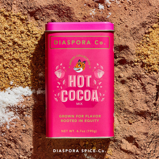 Diaspora Spices Co. Hot Cocoa Mix tin on cocoa powder, showcasing Grown for Flavor, Rooted in Equity label with tiger illustration, promising velvety, naturally-sweetened hot chocolate.
