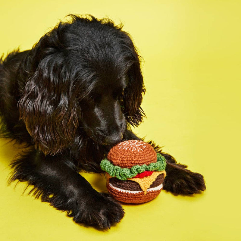 Ware of the Dog - Hand Knit Hamburger Dog Toy being inspected by a black spaniel-type dog, showcasing its intricate lambswool crochet design with squeaker feature.