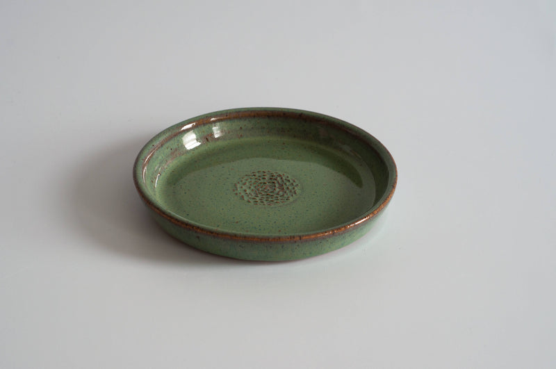 RachaelPots - Garlic Scraper: Sage, a speckled green ceramic dish with textured center for creating garlic puree, sits on a white surface. Handcrafted stoneware made in Brooklyn.