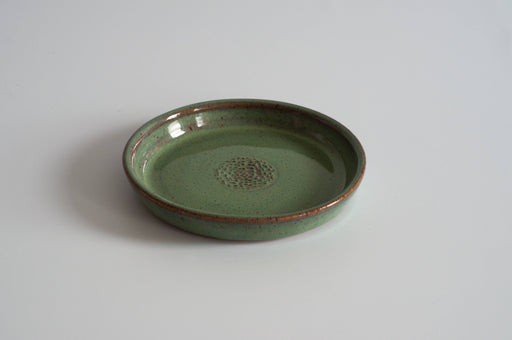 RachaelPots - Garlic Scraper: Sage, a speckled green ceramic dish with textured center for creating garlic puree, sits on a white surface. Handcrafted stoneware made in Brooklyn.