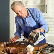Older man in kitchen using Hestan | Titanium Essential 5-Piece Cookware Set to pour sauce onto roast, showcasing its precision and durability.