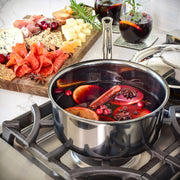 Hestan NanoBond 4qt Saucepan with mulled wine, featuring orange slices, cranberries, and spices on a stovetop, complemented by a charcuterie board and mulled wine glasses.