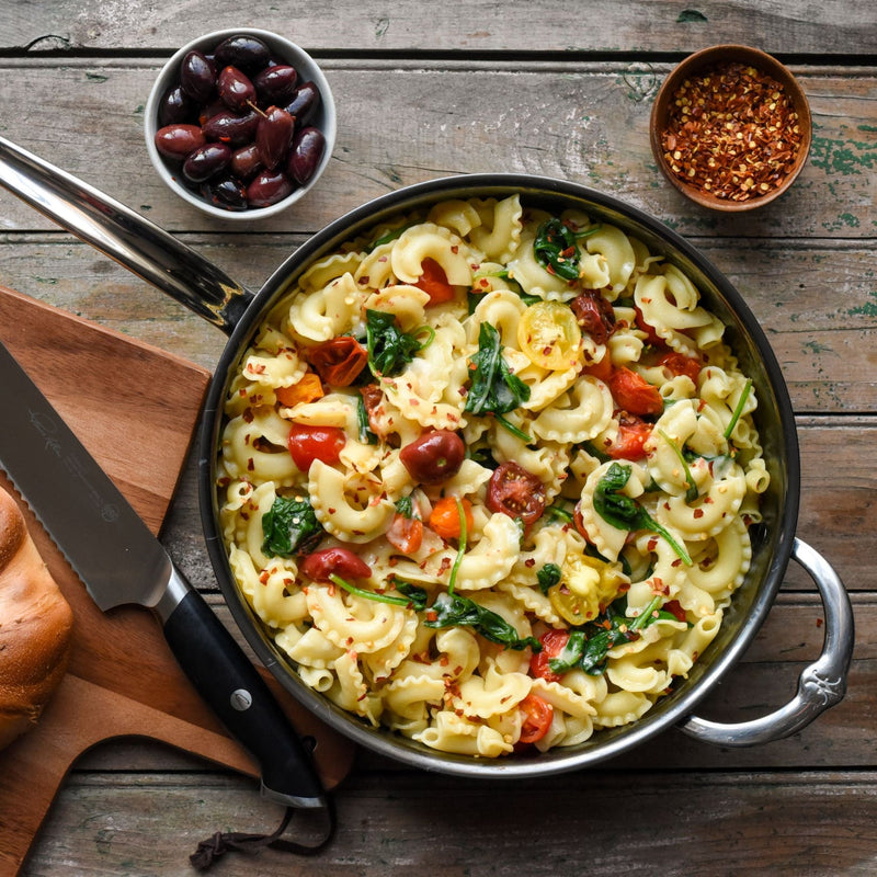 Hestan NanoBond 5qt Sauté Pan filled with Mediterranean-style pasta, showcasing its versatility and durability, surrounded by complementary ingredients for a complete meal experience.