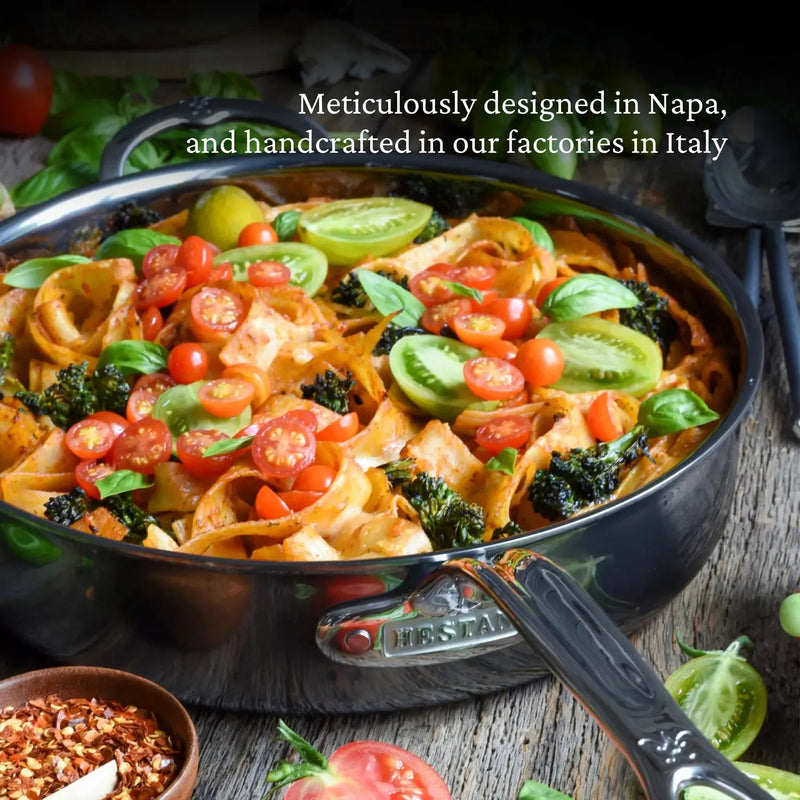 Hestan NanoBond 3.5qt Sauté Pan with ribbon pasta in tomato sauce, topped with tomatoes, broccoli, basil; surrounded by spices and ingredients.