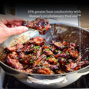 A hand holds chicken in a Hestan Nanobond 14 Wok, showcasing its cooking capabilities, ideal for culinary enthusiasts.