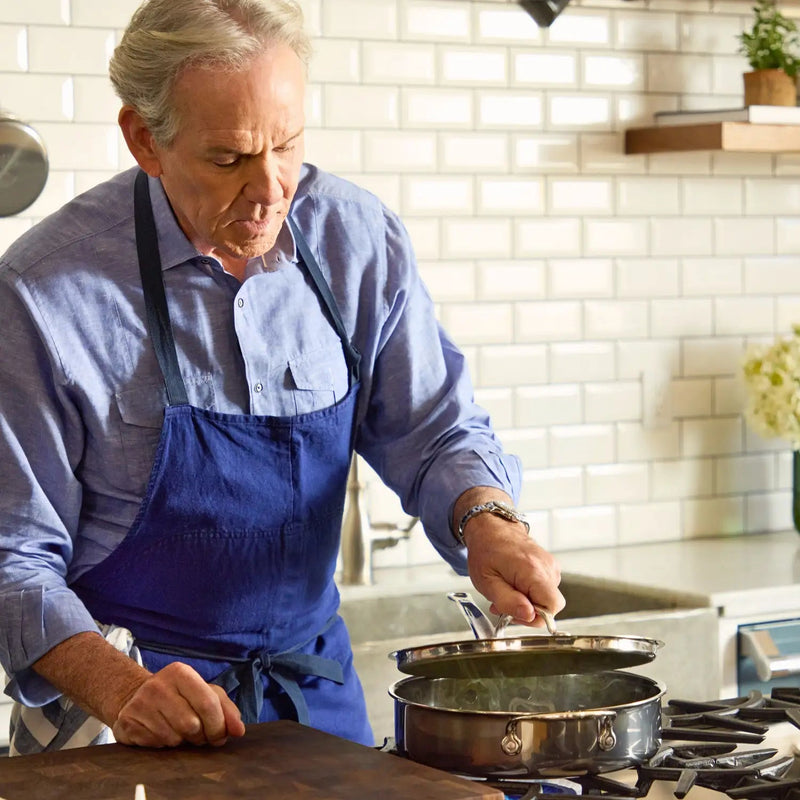 Man checks Hestan | Titanium Essential 5-Piece Cookware Set on stove, showcasing its durability and precision, in a contemporary kitchen setting.