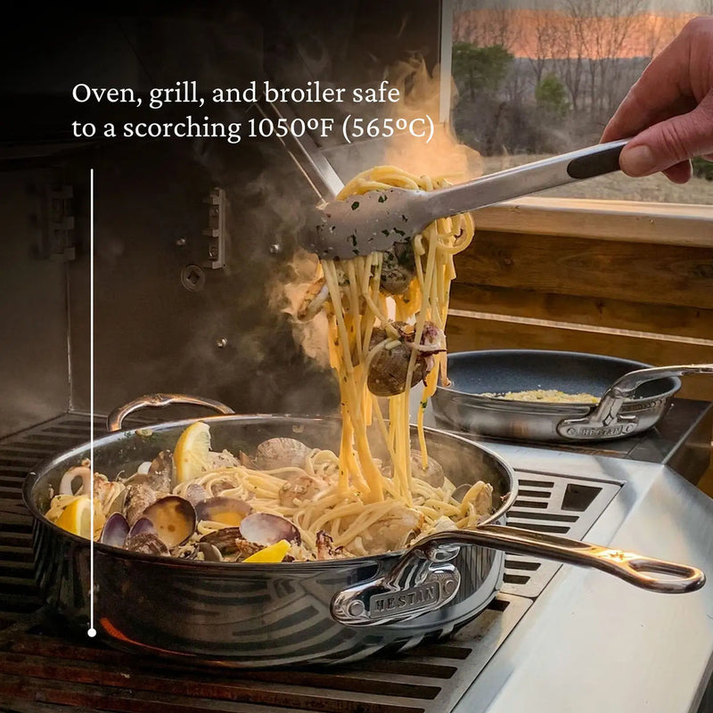 Hestan 3.5qt Sauté Pan filled with seafood pasta on grill, showcasing versatility and durability up to 1050°F, with ergonomic handle and drip-free pour.