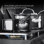 Hestan Titanium Essential 5-Piece Cookware Set on a gas burner, showcasing stainless steel construction with engraved handle, highlighting its durability and high heat resistance.