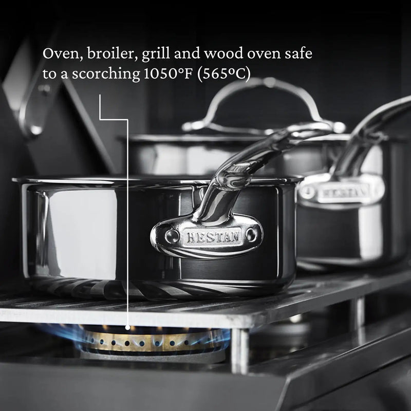 Hestan Titanium Essential 5-Piece Cookware Set on a gas burner, showcasing stainless steel construction with engraved handle, highlighting its durability and high heat resistance.