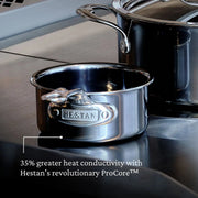 Hestan | Cookware, .75qt Butter Warmer Pan on stovetop, showcases superior heat conduction with ProCore™, alongside larger Hestan stockpot with glass lid.