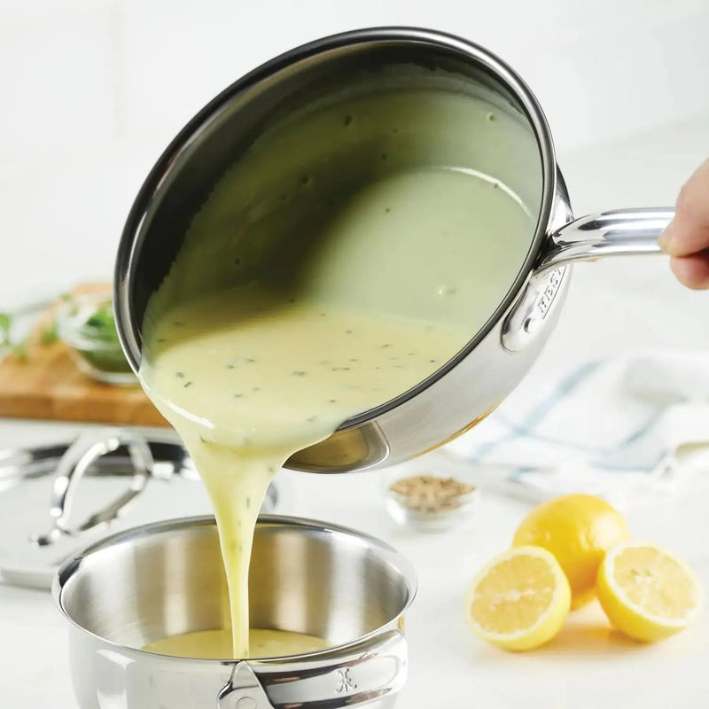 Hestan NanoBond | Cookware, 2qt Saucier Pan + Lid pouring sauce, showcasing its precision pouring design and durable titanium-enhanced stainless steel surface, ideal for sauces.