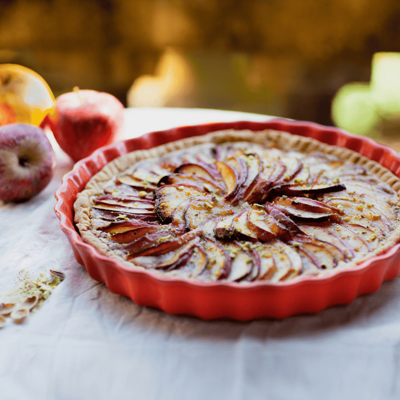 Emile Henry | Deep Flan & Tart Dish, 1.3QT / Cedar, showcasing a beautifully baked apple tart with a golden crust and pistachio garnish in a red fluted pan.