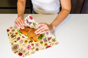 Wrapping a sandwich in a floral Bee's Wrap - Sandwich Wrap - Meadow Magic, showcasing reusable, vegan wax design for sustainable storage from Athens Cooks kitchen store.