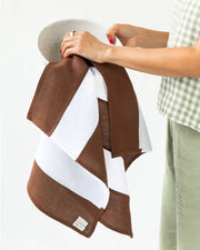 Person holding MagicLinen's Striped Linen Tea Towel, featuring brown and white stripes, designed for zero-waste kitchen use with a convenient hanging loop.