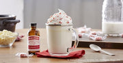 Glass mug with whipped cream and peppermint topping featuring Nielsen-Massey Pure Organic Peppermint, ideal for enhancing desserts or beverages.