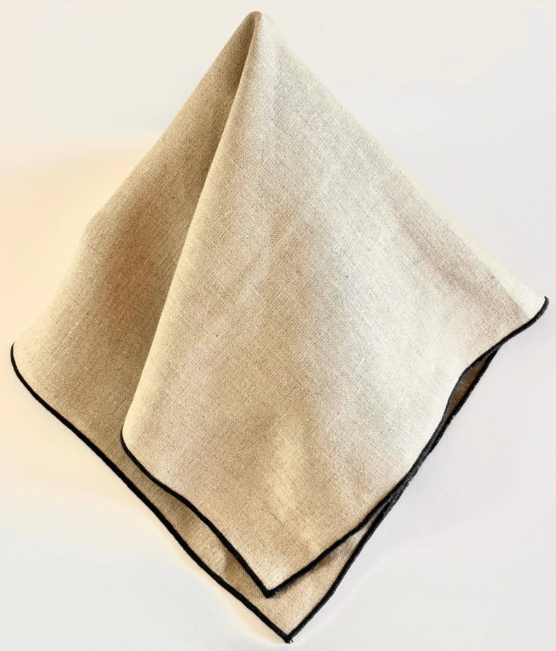 Tisch New York - Napkins, Natural Linen (Black Hem), elegantly folded showcasing its light-beige linen blend with dark stitched border. Set of four, perfect for kitchen elegance.