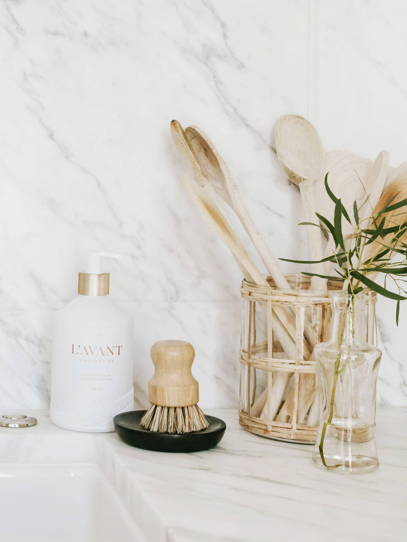 L'AVANT Collective - Fresh Linen High Performing Dish Soap in a stylish matte white glass bottle, accompanied by wooden kitchen utensils and a glass vase.