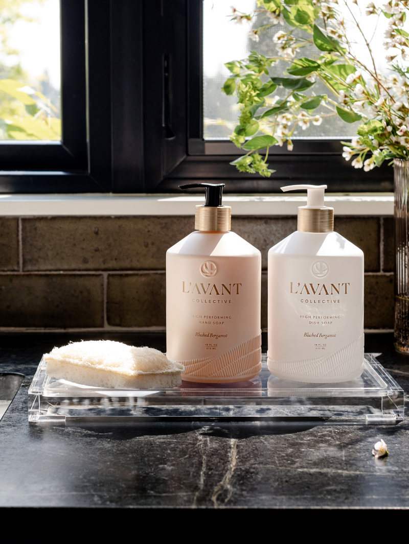 L'AVANT Collective - High Performing Hand Soap - Blushed Bergamot bottles on a counter with a sponge, highlighting elegant design and luxurious scent for a refined washing experience.