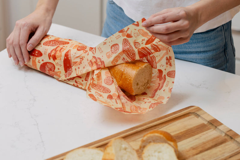 Bee's Wrap - Bread Wrap - Mushroom Magic, Limited Edition: A baguette wrapped in a reusable, beeswax-infused cloth with a mushroom motif, on a kitchen countertop.