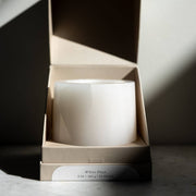 Last Candle Co - White Onyx Refillable Candle in a smooth stone vessel, partially open in a beige gift box, on a marble surface.