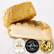 Perrystead Dairy - Atlantis cheese, featuring a mottled yellow-orange rind and creamy ivory interior, with award seals for American Cheese Society, World Cheese Awards, and World Championship Cheese.