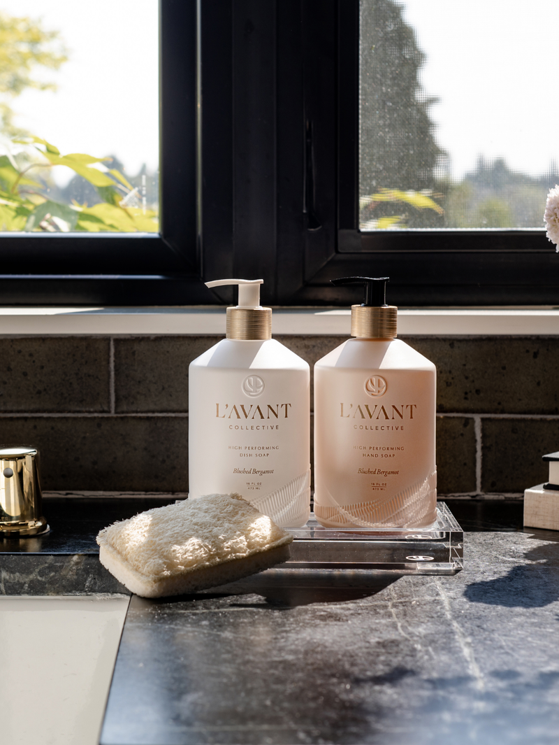 L'AVANT Collective - High Performing Dish Soap - Blushed Bergamot in a matte white glass bottle on a countertop, complemented by a white sponge nearby.