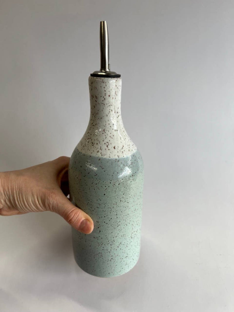 Hand holding the RachaelPots - Oil Cruet Large: Nude/White, a handmade ceramic bottle with a pour spout, ideal for olive oil use.