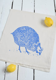 Hearth and Harrow - Organic Cotton Guinea Hen Tea Towel in Blue-violet, featuring a blue-violet Guinea Hen design, displayed with a lemon. Ideal for kitchen use.