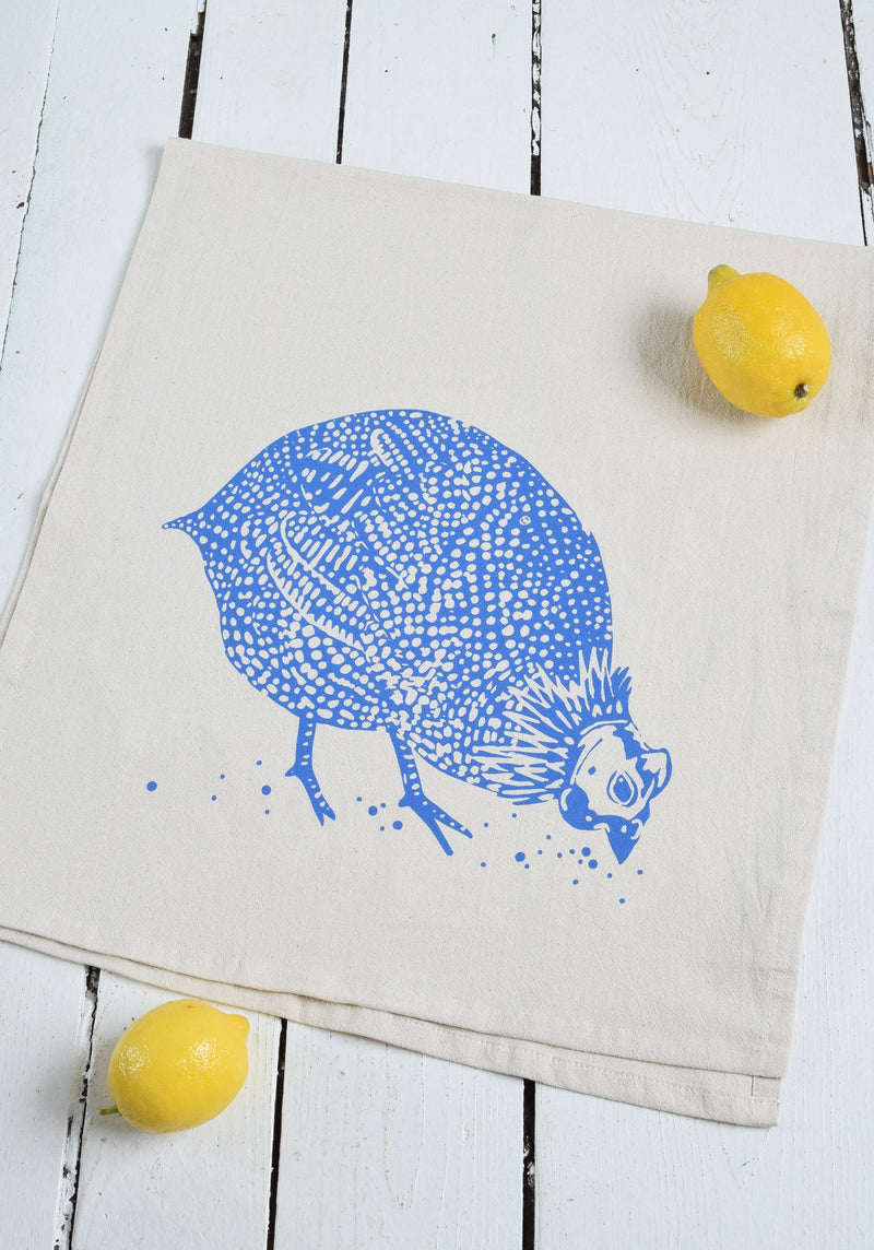 Hearth and Harrow - Organic Cotton Guinea Hen Tea Towel in Blue-violet, featuring a blue-violet Guinea Hen design, displayed with a lemon. Ideal for kitchen use.