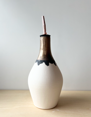 Jessica Wertz Ceramics Gold + White Oil Bottle: A 10 tall unglazed off-white vessel with a bronze-glazed neck, featuring a black stopper and rose-gold straw.