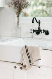 Caravan Home | Vintage Linen Natural & Black Towels elegantly draped over a farmhouse sink, showcasing rustic charm with their handcrafted design. Perfect for any kitchen setting.