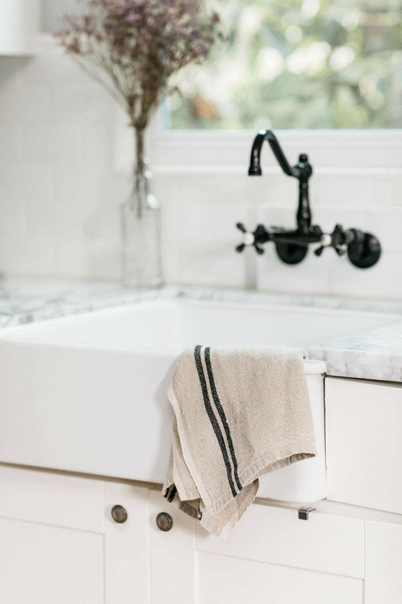 Caravan Home | Vintage Linen Natural & Black Towels elegantly draped over a farmhouse sink, showcasing rustic charm with their handcrafted design. Perfect for any kitchen setting.