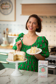 Woman in kitchen holding a plate with a slice of layered sprinkle cake, showcasing Hayden Flour Mills - Molly Yeh x HFM Confetti Cake Mix on counter.