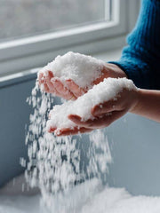 Hands gently release HAVSNØ Fine Kosher Norwegian Sea Salt, resembling snowflakes, into a container, showcasing its purity and culinary versatility for home cooks.