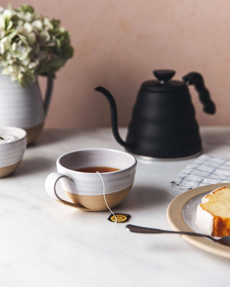 Farmhouse Pottery - Pantry Mug: Large, filled with tea, on a serene tea-time setup with pound cake, kettle, and hydrangeas, embodying a cozy, minimalist vibe.